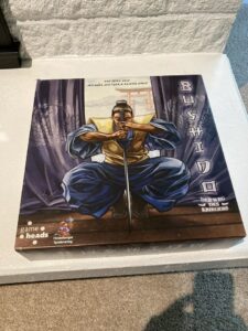 A boxed board game called "Bushido" featuring an illustrated samurai kneeling with a pair of swords crossed in front of him on the cover. The text includes the game designers' names and a tag from the publisher "Heidelberger Spieleverlag."