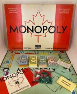 Vintage Canadian edition Monopoly board game laid out with box, money, cards, and plastic houses and hotels.