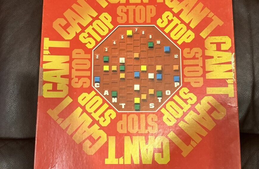 A worn board game box titled "CAN'T STOP" with a red and orange color scheme lying on a leather surface, and the tagline "HOW FAR CAN YOU PUSH YOUR LUCK?" at the bottom.