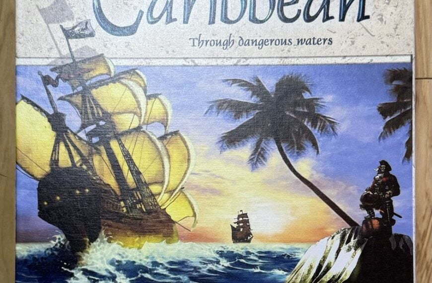 Box cover of the "Caribbean" board game featuring a large sailing ship on turbulent seas with smaller ships in the background, a tropical setting with palm trees, and a pirate figure on a rock in the foreground. The text on the cover includes the game's title and subtitle 'Through dangerous waters' and the names 'Michail Antonow' and 'Jens-Peter Schliemann' with the 'Rio Grande Games' logo at the bottom right.