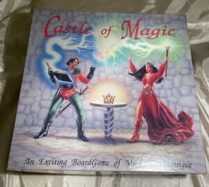 A board game titled "Castle of Magic" featuring artwork with two fantasy characters — one reading from a magical book with energy emanating from it, and the other, a female figure, holding a staff with a swirling magical aura above. A crown on a pedestal appears in the center, all set against a stone floor and a mystical blue and green cloudy background. The subtitle reads, "An Exciting Board Game of Magic & Intrigue."