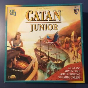 Box cover for the "CATAN Junior" board game showing a boy and a girl looking out to sea with a parrot flying overhead, a harbor scene with ships in the background, and text describing it as "A CATAN Adventure for Fledgling Swashbucklers."