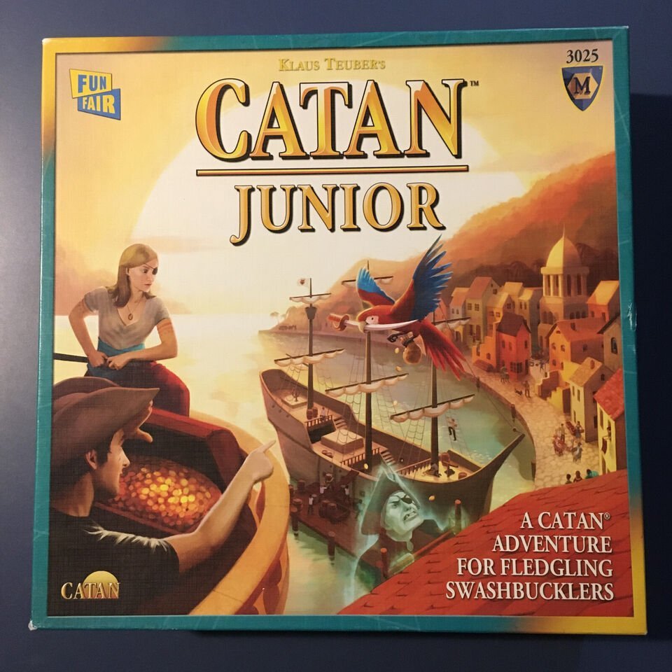 Box cover for the "CATAN Junior" board game showing a boy and a girl looking out to sea with a parrot flying overhead, a harbor scene with ships in the background, and text describing it as "A CATAN Adventure for Fledgling Swashbucklers."