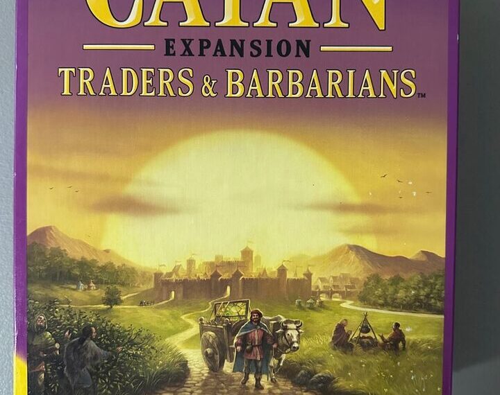 Box cover of "Klaus Teuber's Catan Expansion: Traders & Barbarians" board game, featuring illustrated medieval characters on a road leading to a fortified city.
