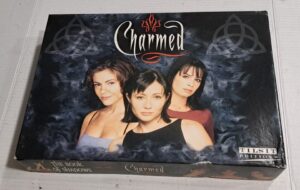A boxed set of "Charmed: The Book of Shadows" board game with images of the three main characters on the cover, surrounded by cloudy blue smoke and mystical symbols.