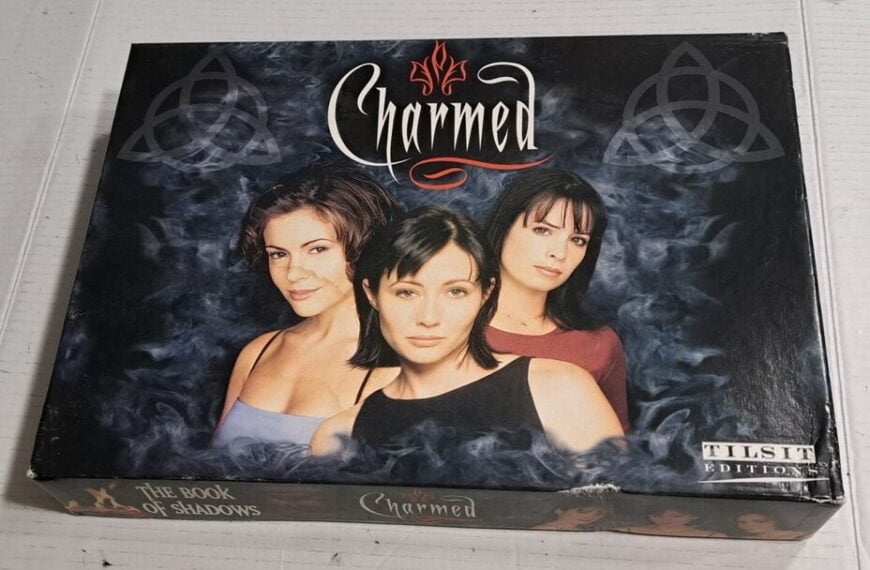 A boxed set of "Charmed: The Book of Shadows" board game with images of the three main characters on the cover, surrounded by cloudy blue smoke and mystical symbols.