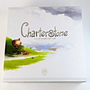 A box cover for the board game "Charterstone," which is described as a village-building legacy game designed by Jamey Stegmaier, with artwork depicting a green landscape, floating islands, and a brass-colored airship. The game is produced by Stonemaier Games.