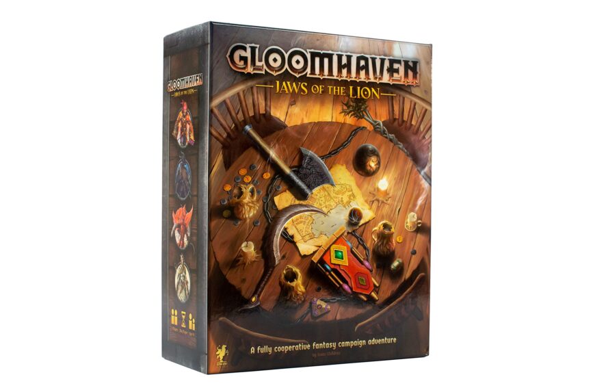 Gloomhaven: Jaws of the Lion board game box, featuring fantasy artwork of weapons, a map, and various objects on a wooden table.