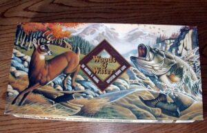 Board game box titled "Woods & Water" featuring artwork of a deer and a large fish in a riverine and forest setting.