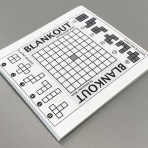 Blankout puzzle book on a gray surface showing a grid and small shape blocks to be arranged.