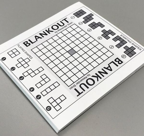 Blankout puzzle book on a gray surface showing a grid and small shape blocks to be arranged.