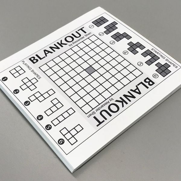 Blankout puzzle book on a gray surface showing a grid and small shape blocks to be arranged.