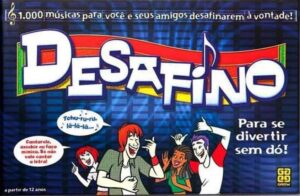 Board game cover titled "DESAFINO" featuring cartoon illustrations of four people singing and enjoying themselves with musical notes and text bubbles, advertising 1,000 songs for fun challenges.